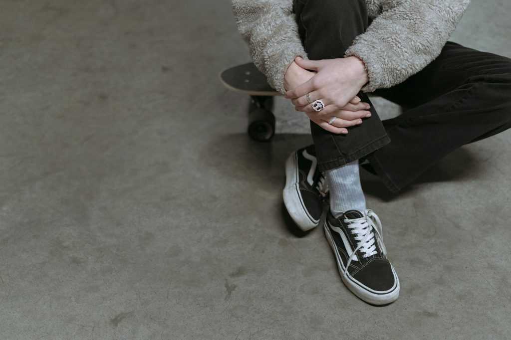 Stylish skater sitting on a skateboard wearing classic sneakers indoors.